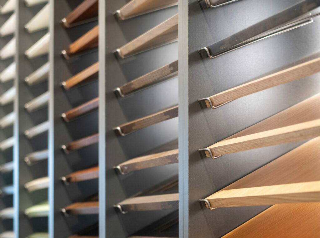 Close-up view of cabinet door samples displayed in rows, showcasing a variety of wood tones and painted finishes at a Merit Kitchens Design Centre.